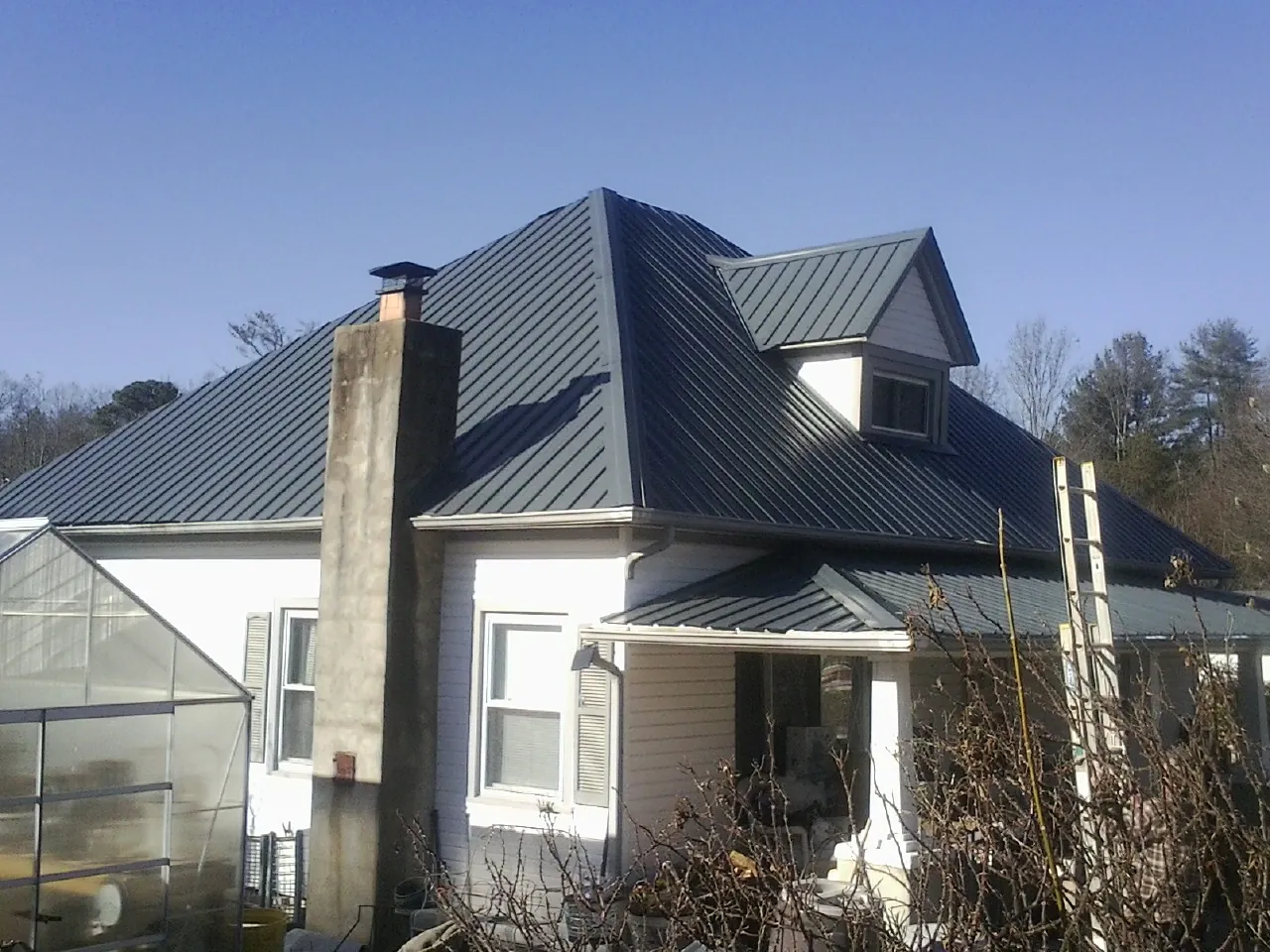 Dark blue standing seam metal roof on a white farmhouse with dormer — Slate & Tile Roof Repair by Roofing Brothers in Hughes Springs