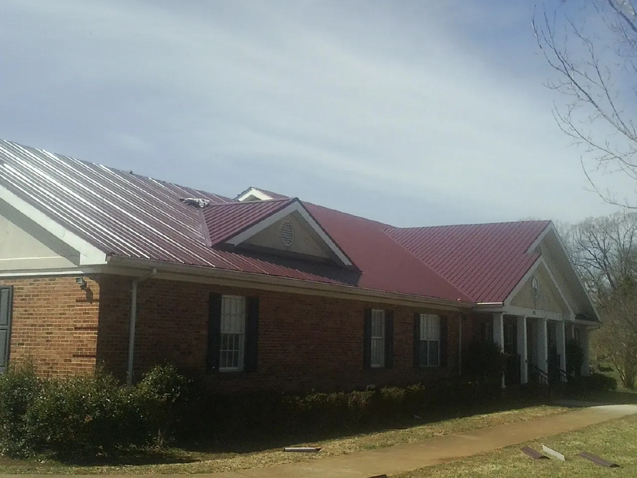 Red metal roof with gabled entries on a long brick building, from a Hail Damage Roof Repair job in Hughes Springs