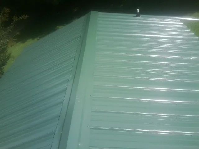 New green metal panels meeting at the ridge of a roof — Flat Roof Repair work by our crew in Hughes Springs