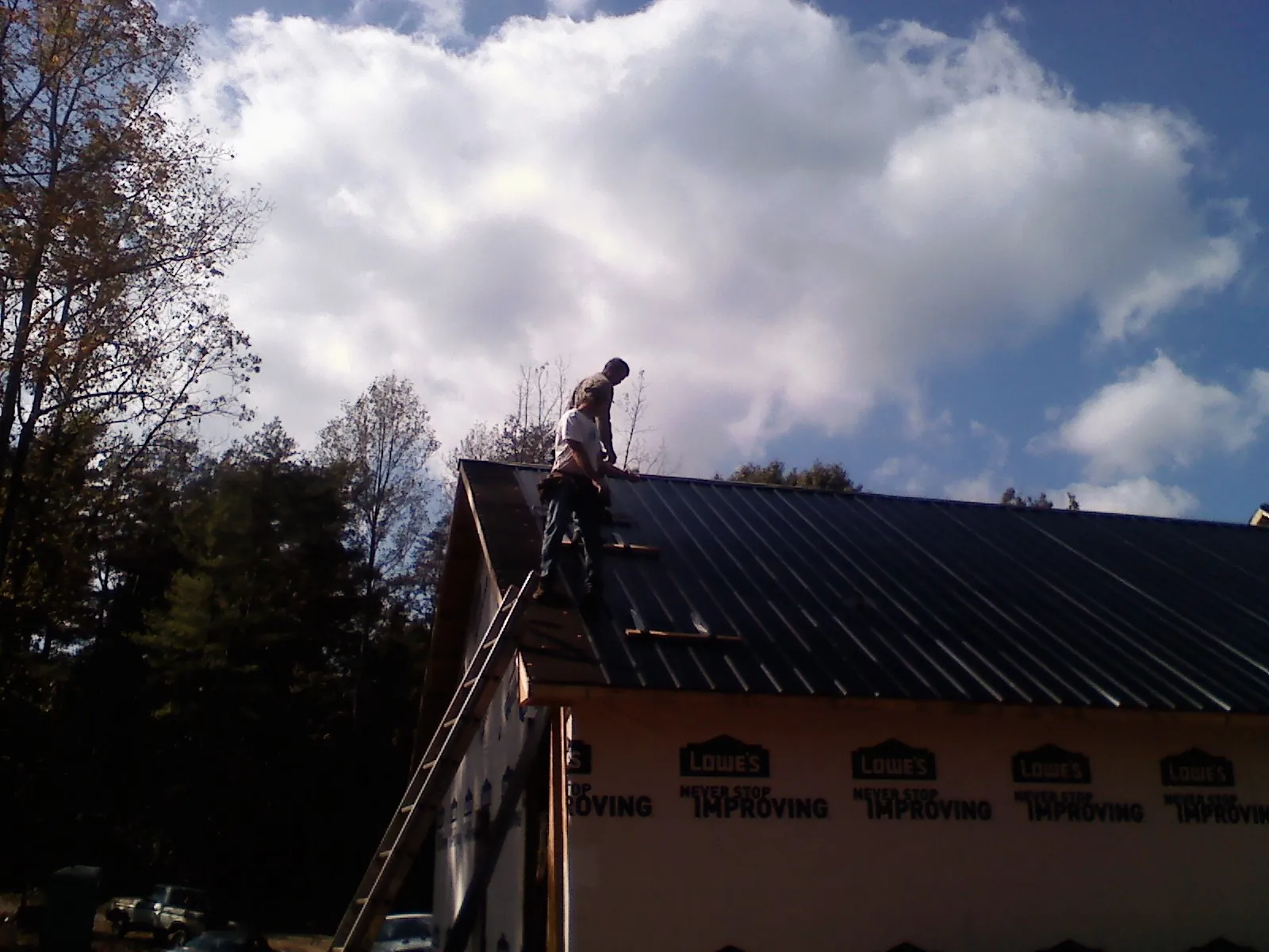 Roofer fastening dark metal panels high against a cloudy sky, from a Roof Inspection job in Hughes Springs