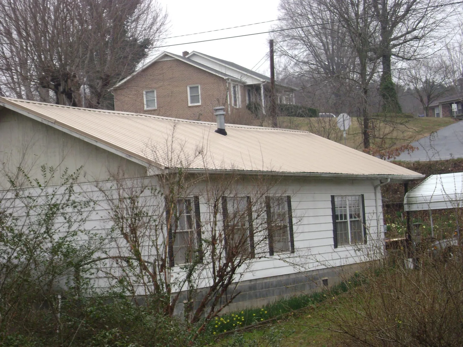 Tan metal roof on a white sided house set into a hillside — Commercial Roofing by Roofing Brothers in Hughes Springs