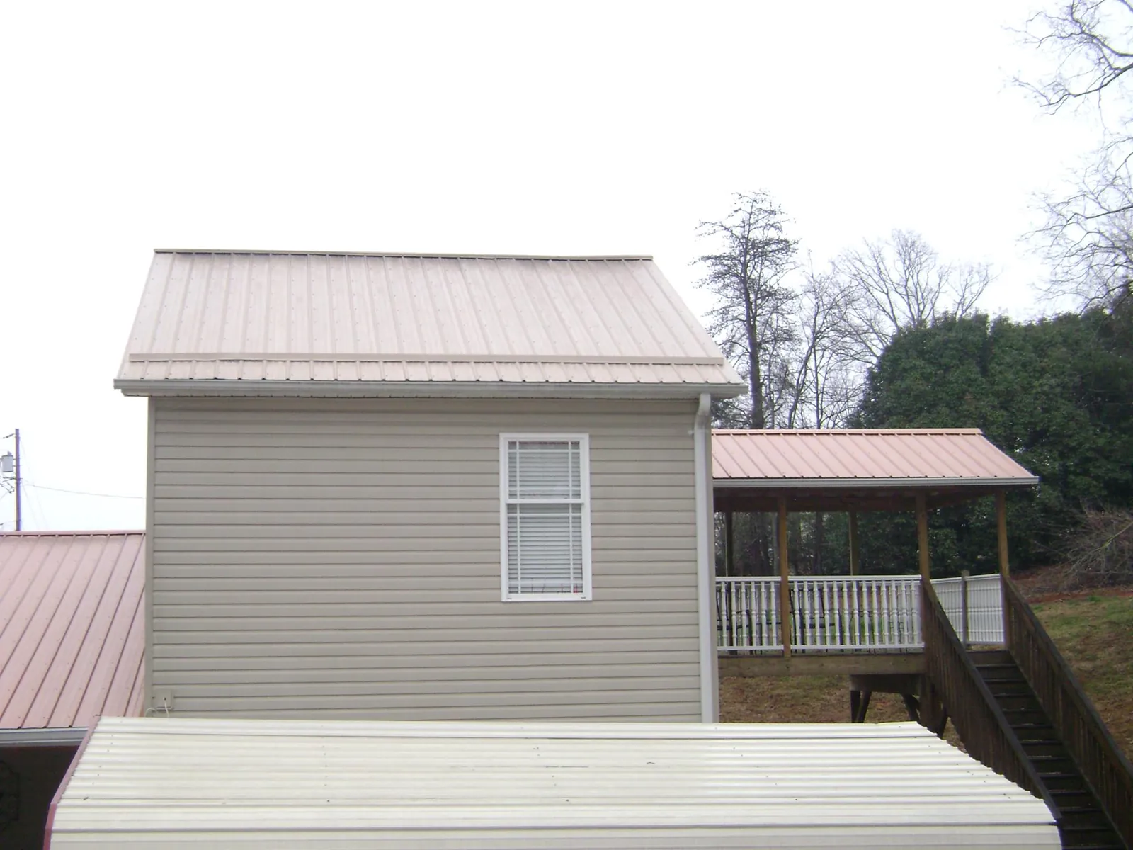 Tan metal roofs on a two story addition and attached porch, from a Roof Replacement job in Hughes Springs